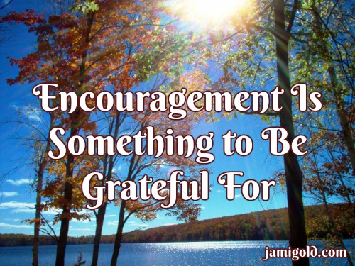 Sun rays over a lake and fall colors with text: Encouragement Is Something to Be Grateful For