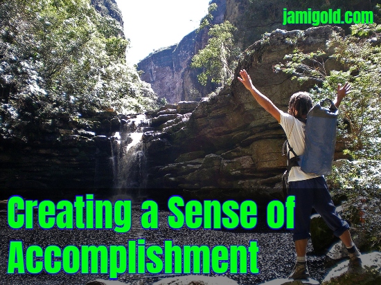Man with arms upraised in front of waterfall with text: Creating a Sense of Accomplishment